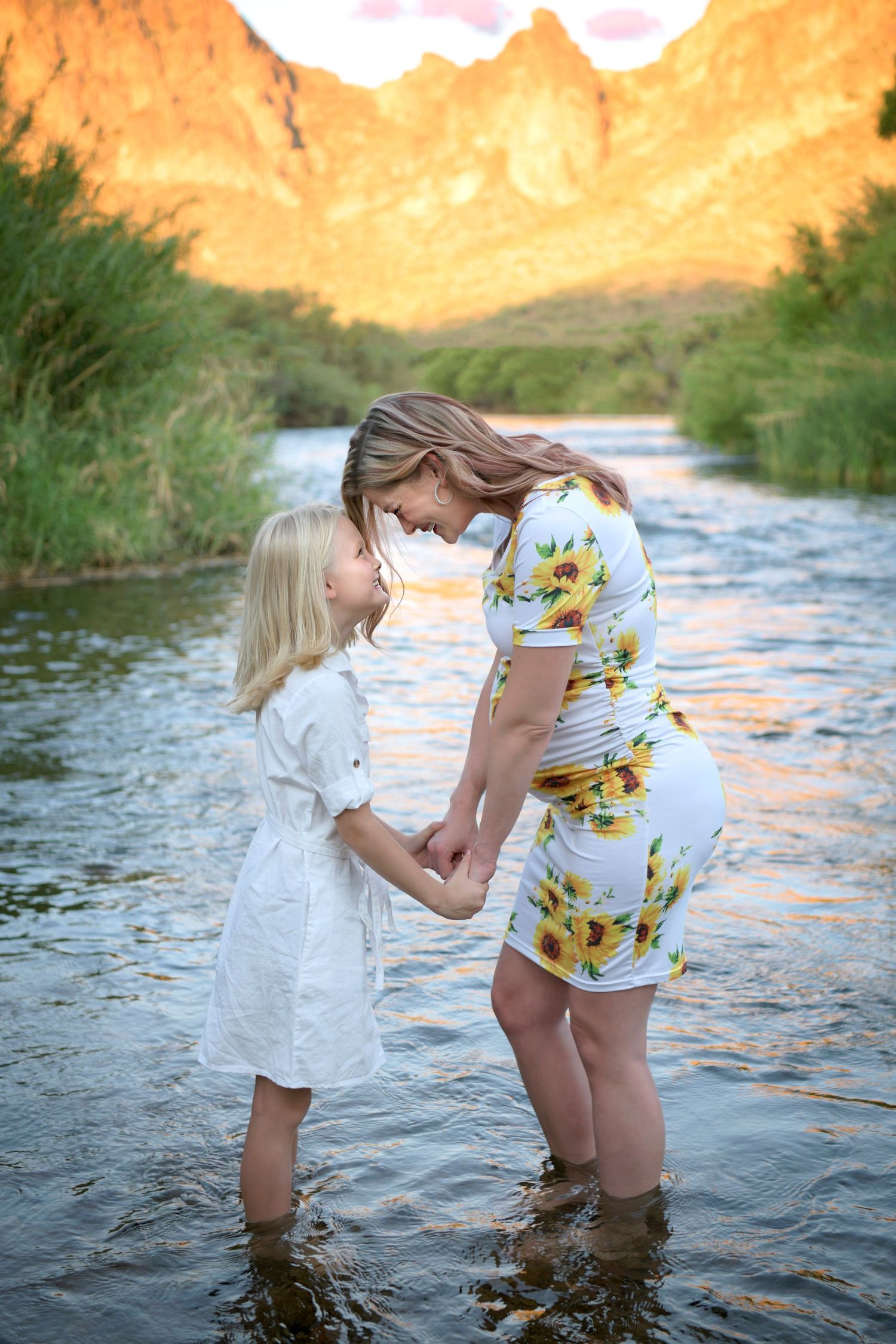 Pregnant woman and daughter in a flowing dress standing in a sunlit desert salt river