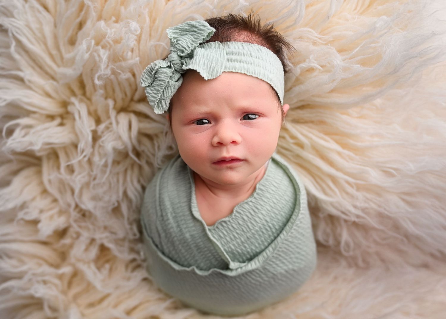 Baby stares intensely right into the camera while laying on a cream flokati rug