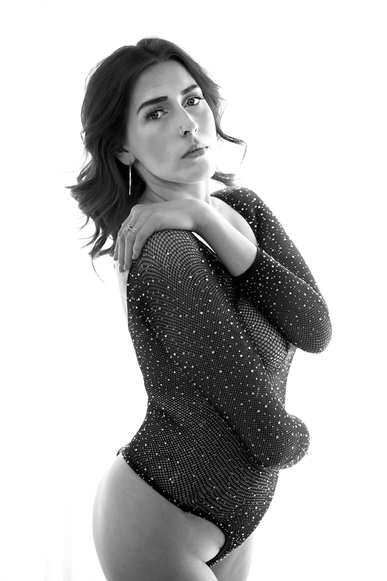 Woman in sparkly bodysuit stands staring at the camera in a black and white boudoir photo