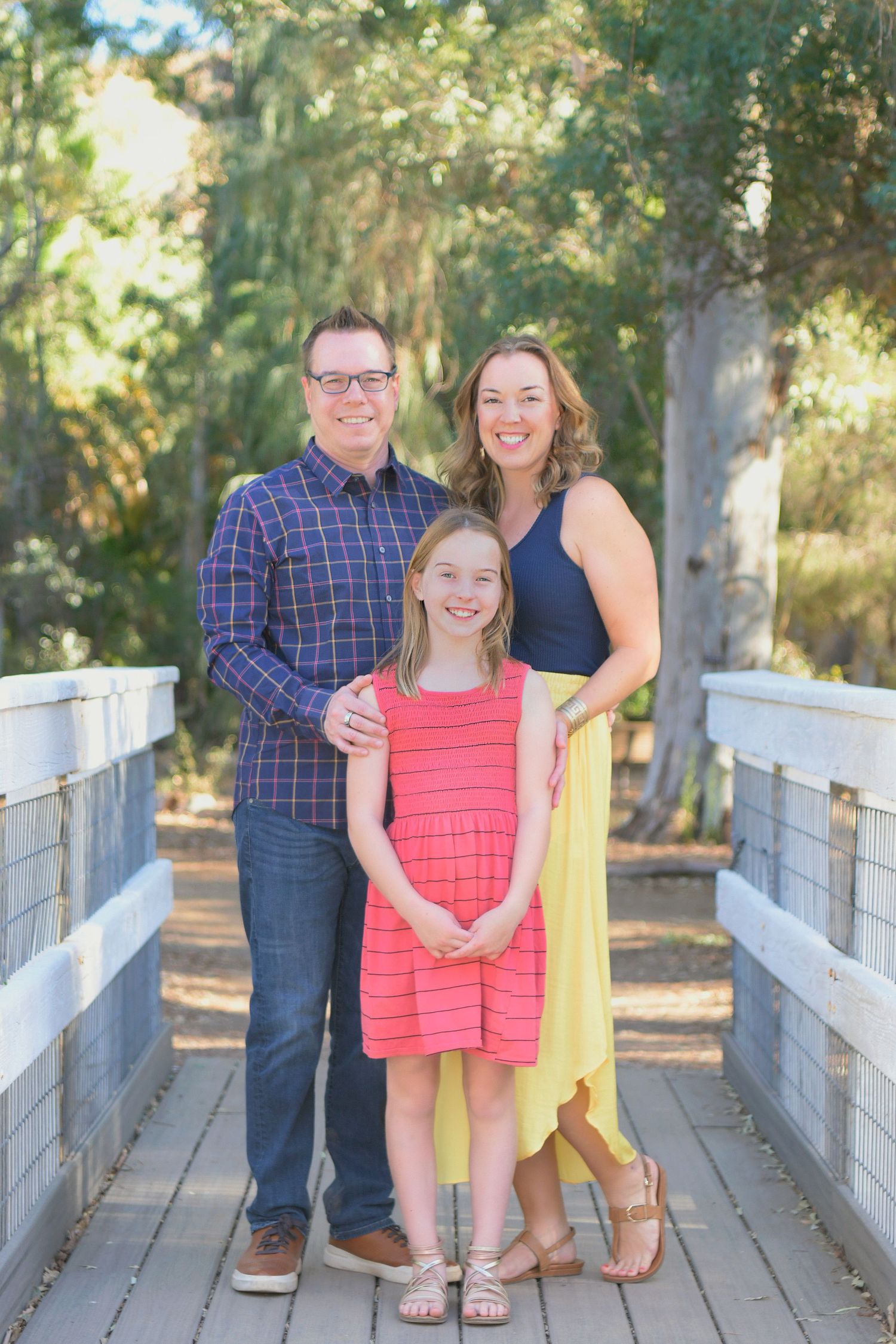 Family of three stands on a white bridge overlooking a Northern Arizona Forest
