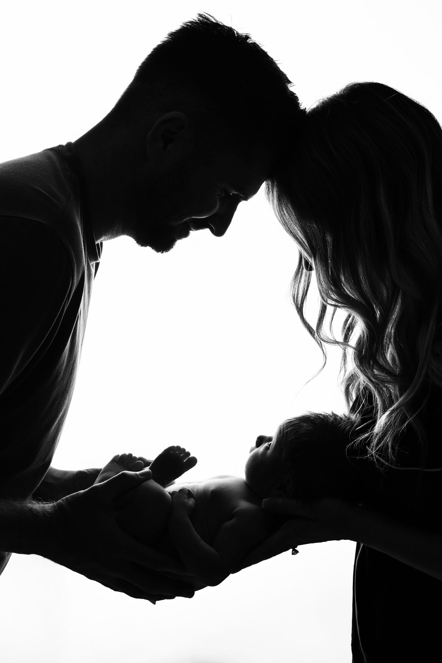 A backlit silhouette of parents holding their newborn baby looking up at them.