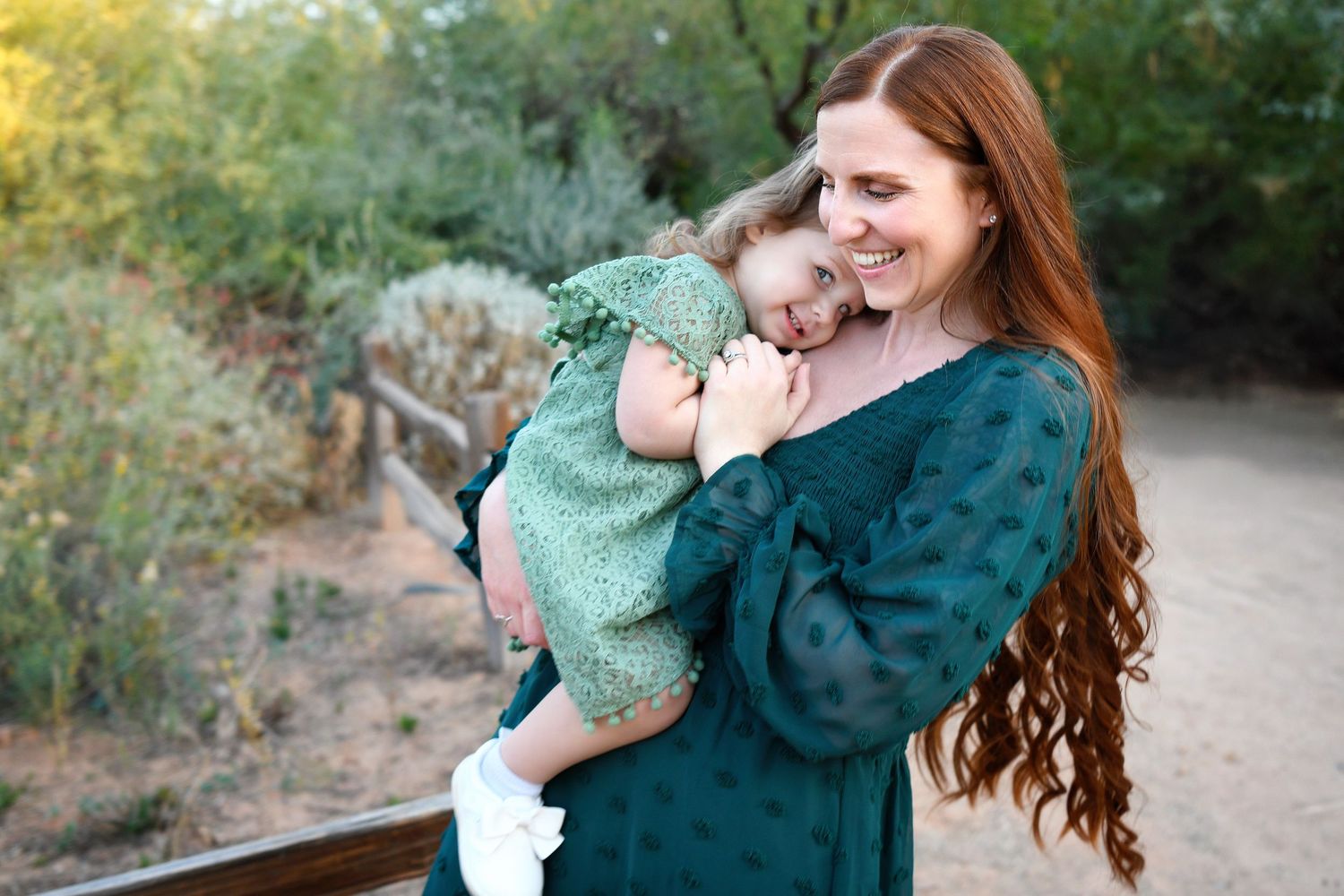 Mother Daughter stand snuggling in green dresses outdoor in Gilbert Arizona Riparian Preserve