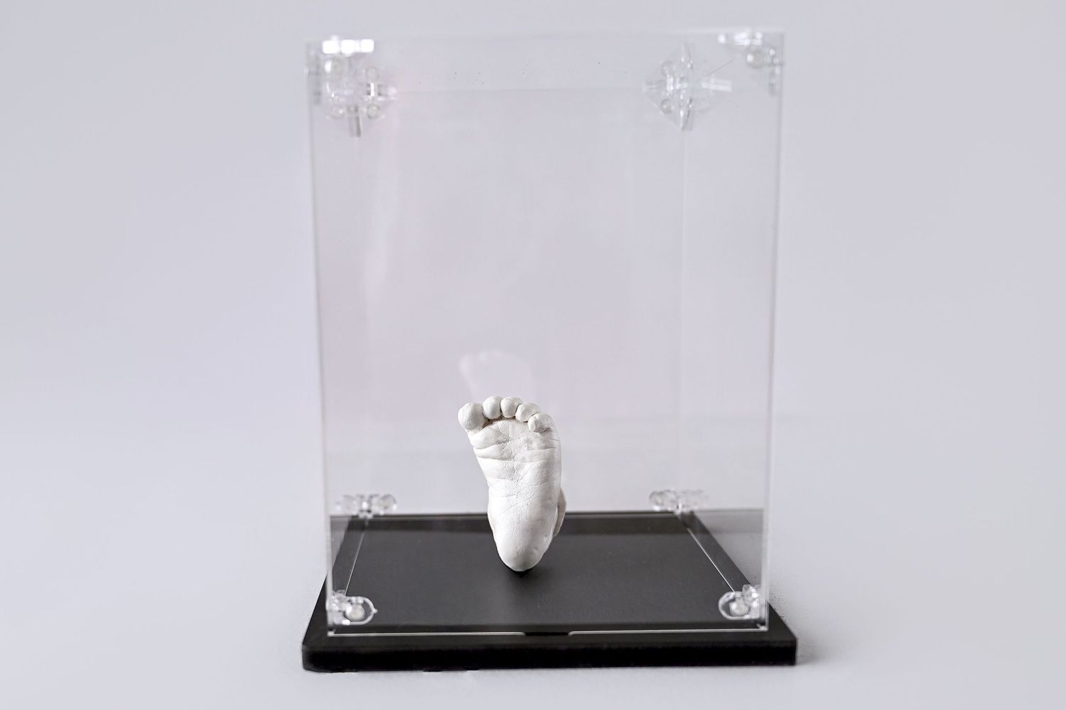 A museum box filled with an acrylic box and a small handmade stone casting of a newborn baby foot