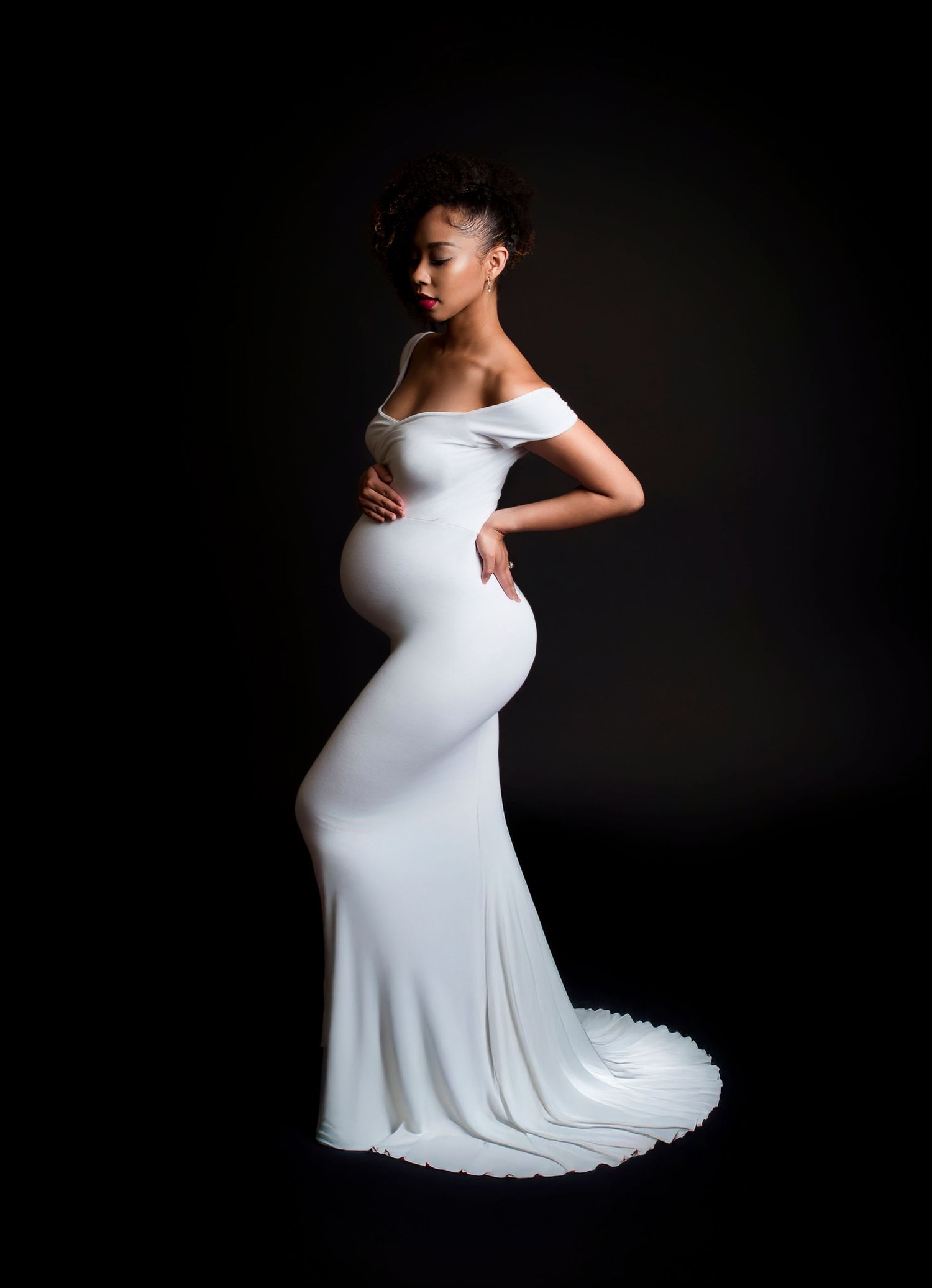side profile image of a pregnant woman standing caressing her belly in a long white gown. High contrast maternity photo in tempe arizona