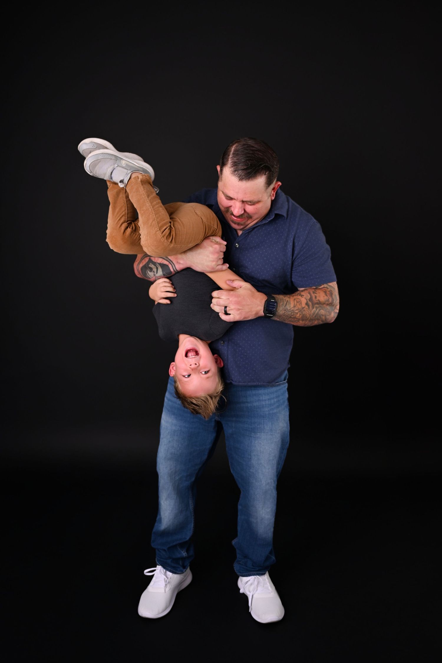Dad holds toddler upside down laughing for Daddy and Me Fathers Day Mini Session In Phoenix Arizona Photography studio