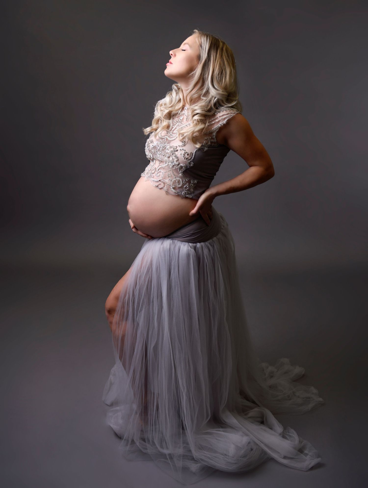 Classic maternity shot in studio with a woman wearing a fitted dress that emphasizes her belly.