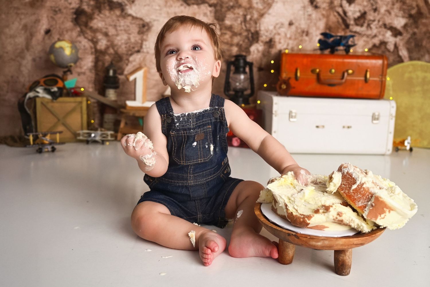 Messy baby boy enjoying his smashed cake in Phoenix studio on a custom vintage travel set.