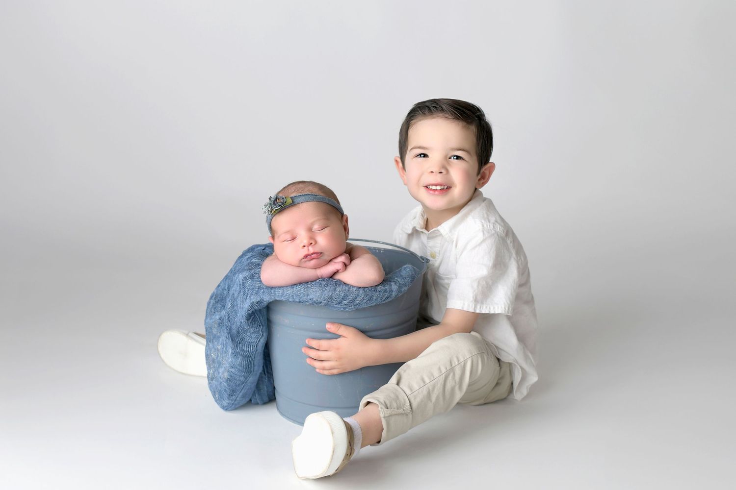Siblings snuggling with newborn baby in bucket for newborn photo in AZ