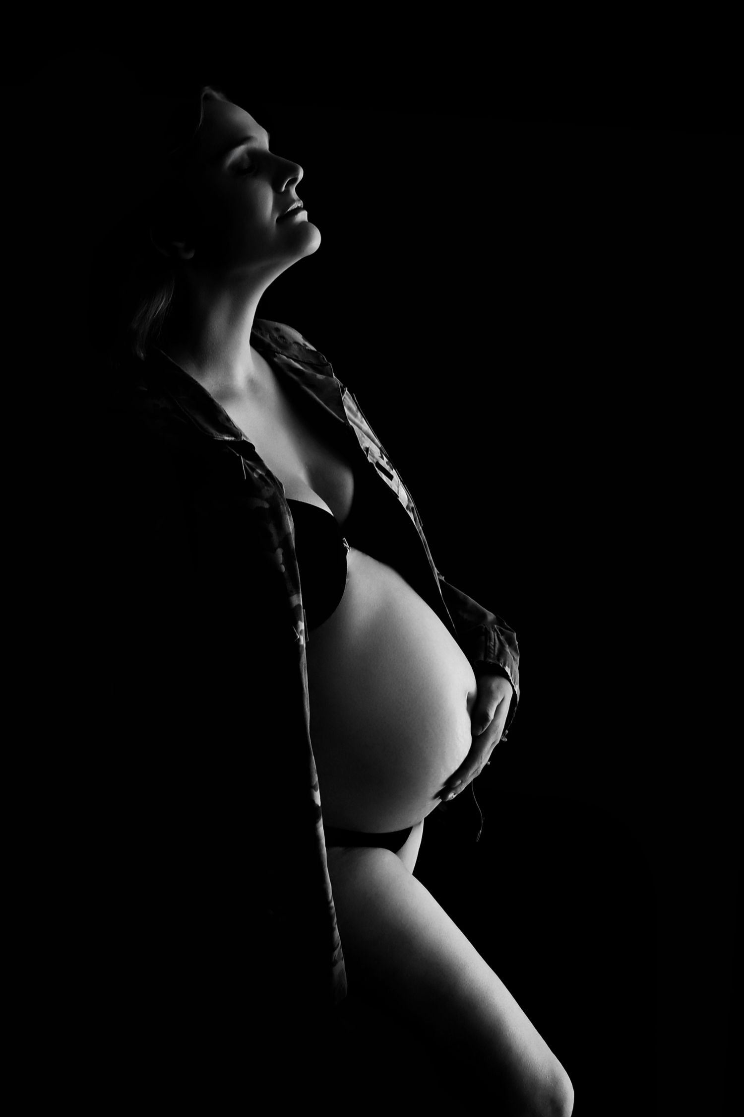 Fine art maternity black and white photo of a pregnant woman posing with the light reflecting off her stomach in Phoenix Photo Studio