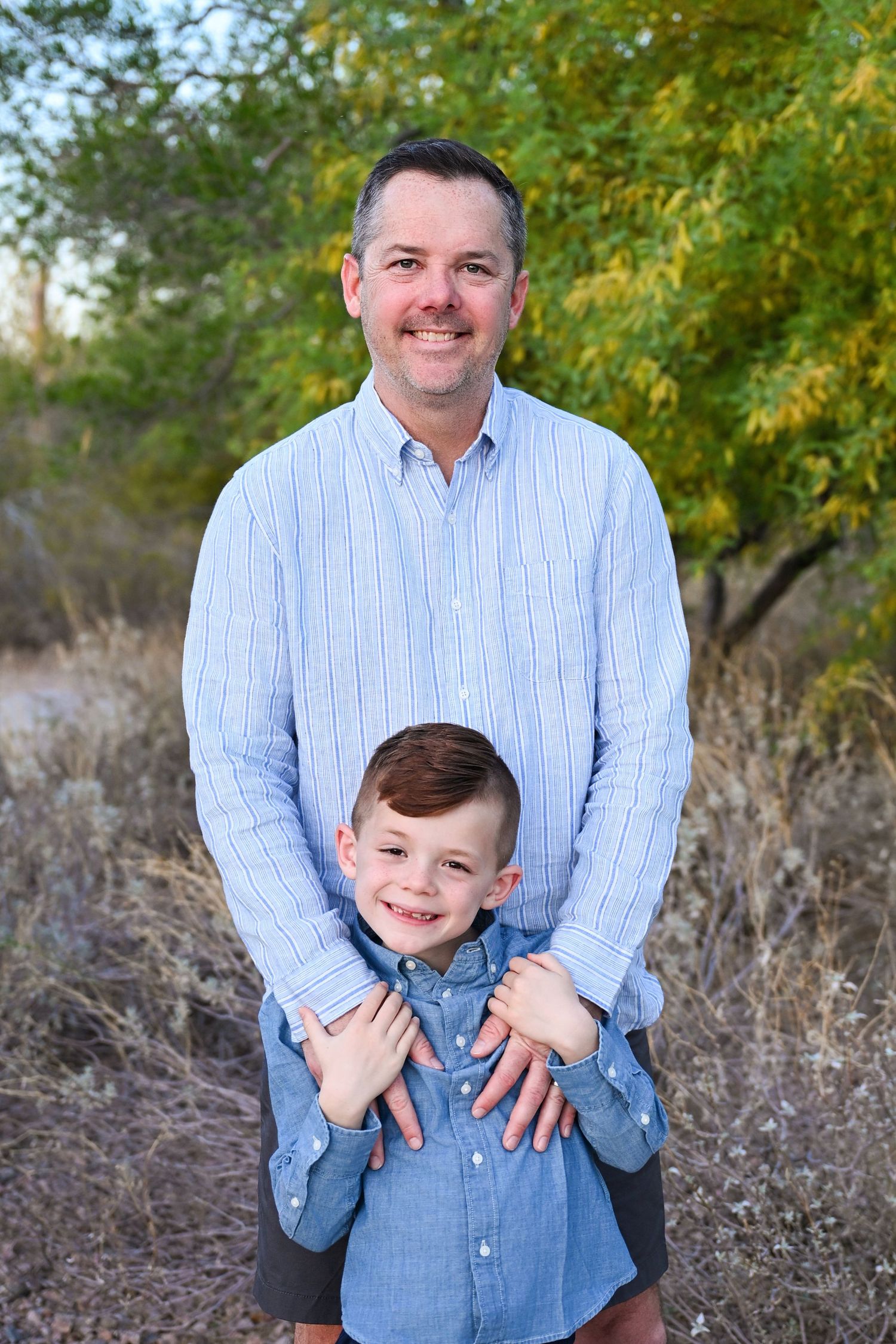 Dad and son stand in matching outfits in Chandler Arizona Park and smile to camera