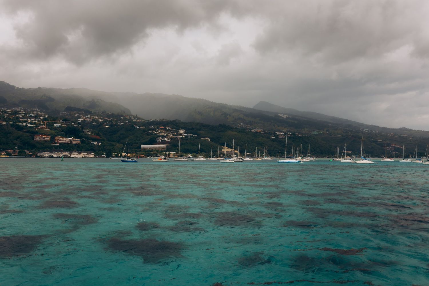 Eaux océaniques tropicales turquoise avec voiliers ancrés près du rivage montagneux d'une île montagneuse.