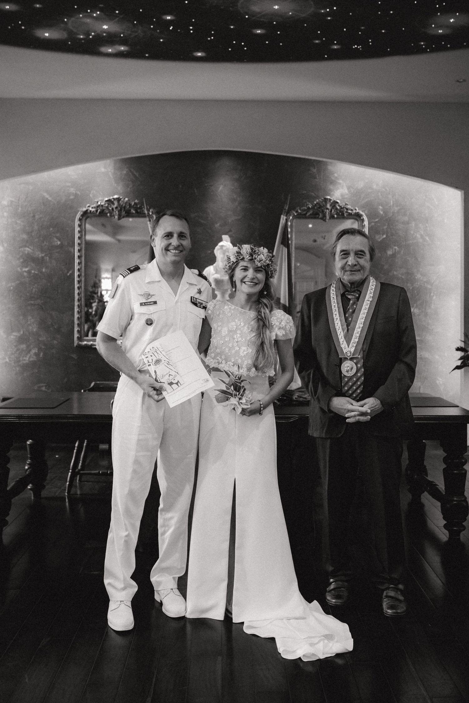 Photo en noir et blanc de la mariée et du marié posant avec l'officier lors de la cérémonie de mariage.
