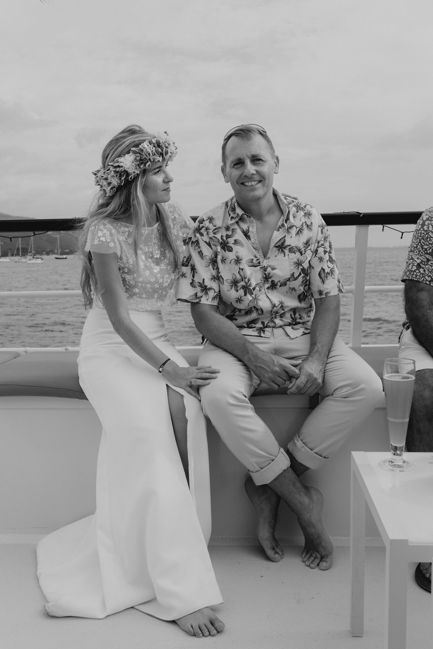 La mariée et le marié en tenue tropicale décontractée sont assis ensemble sur le pont du yacht en noir et blanc.