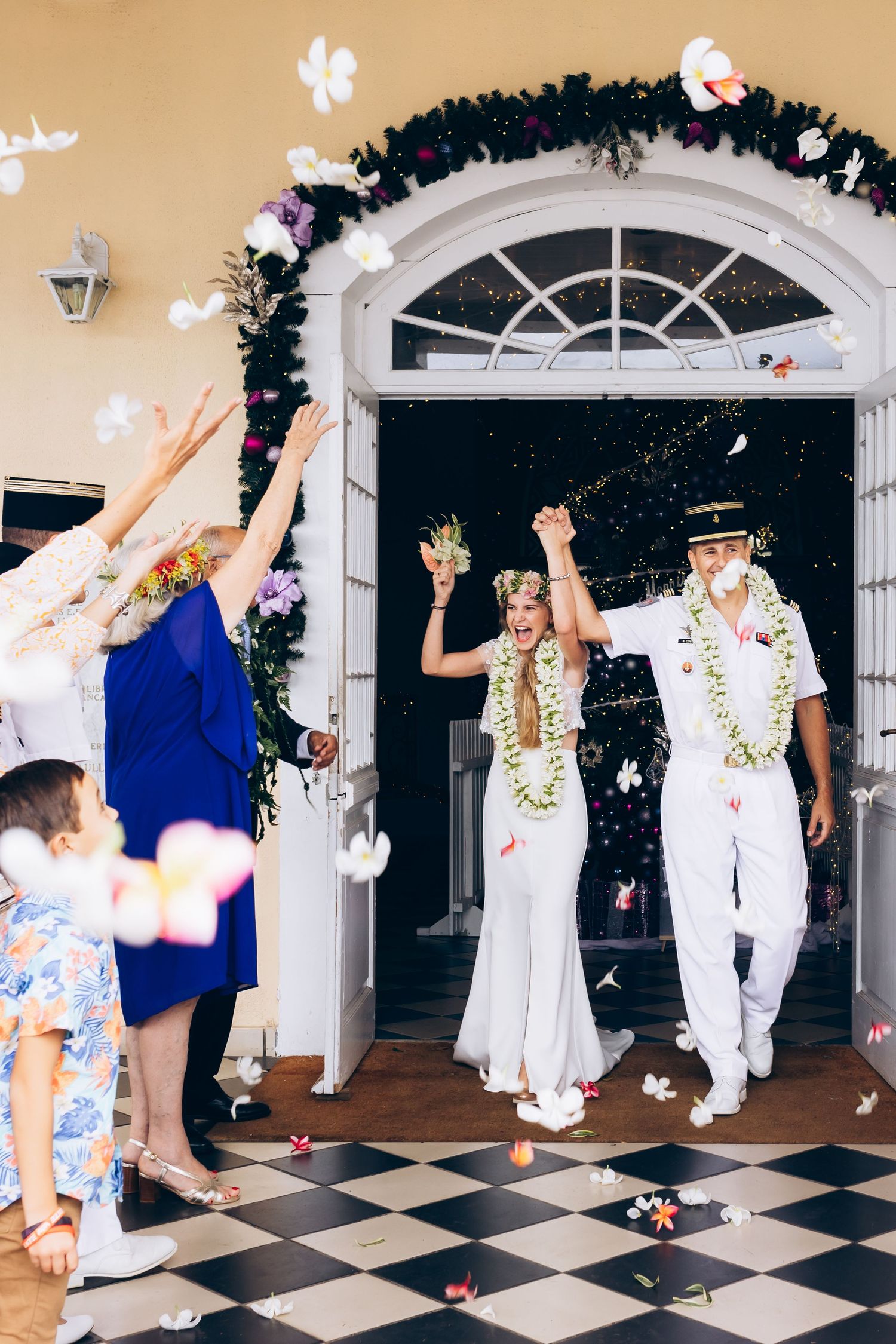 Les joyeux jeunes mariés quittent le lieu de la cérémonie alors que les invités jettent des pétales de fleurs blanches et des confettis