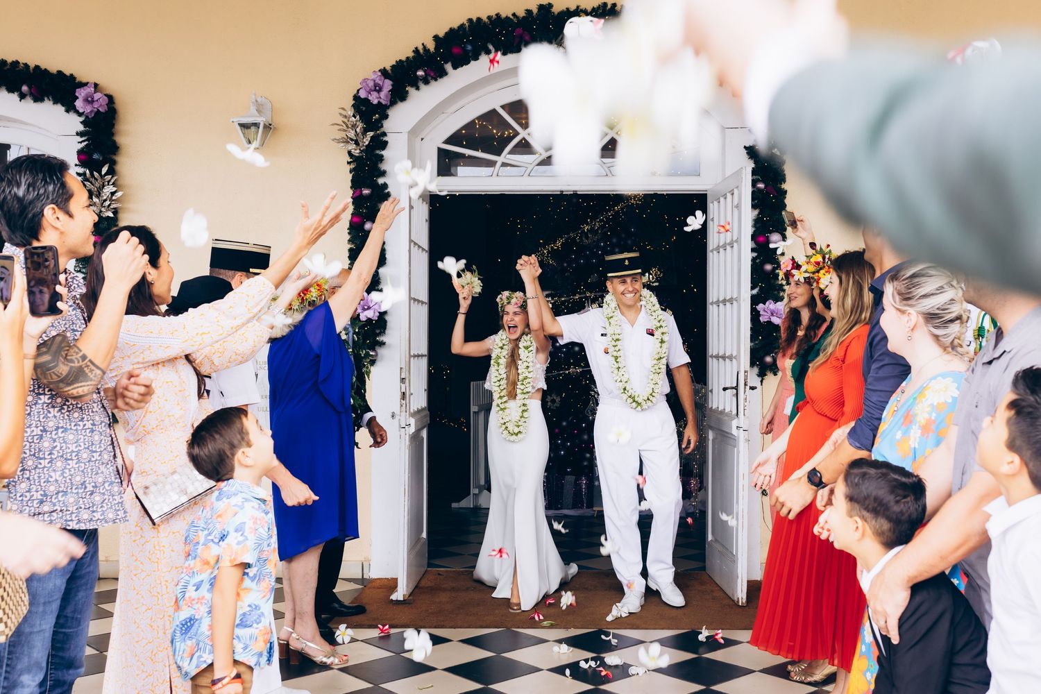 La mariée et le marié dans la porte du lieu décorée de sortie blanche alors que les invités célèbrent avec des confettis et des fleurs.
