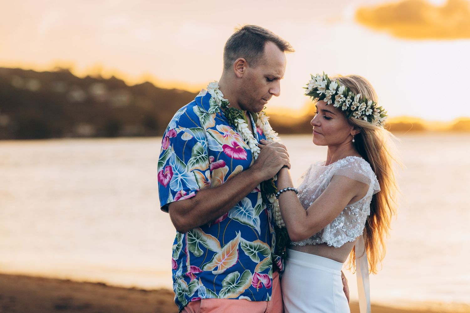Couple romantique en tenue tahitienne partageant un moment tendre sur la plage au coucher du soleil, femme portant une couronne florale.