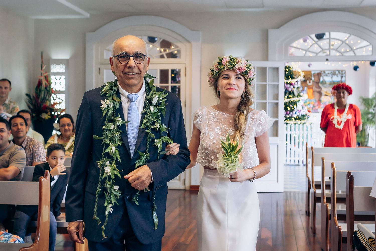 La mariée portant une couronne florale marche dans l'allée avec son père lors d'un mariage tropical.