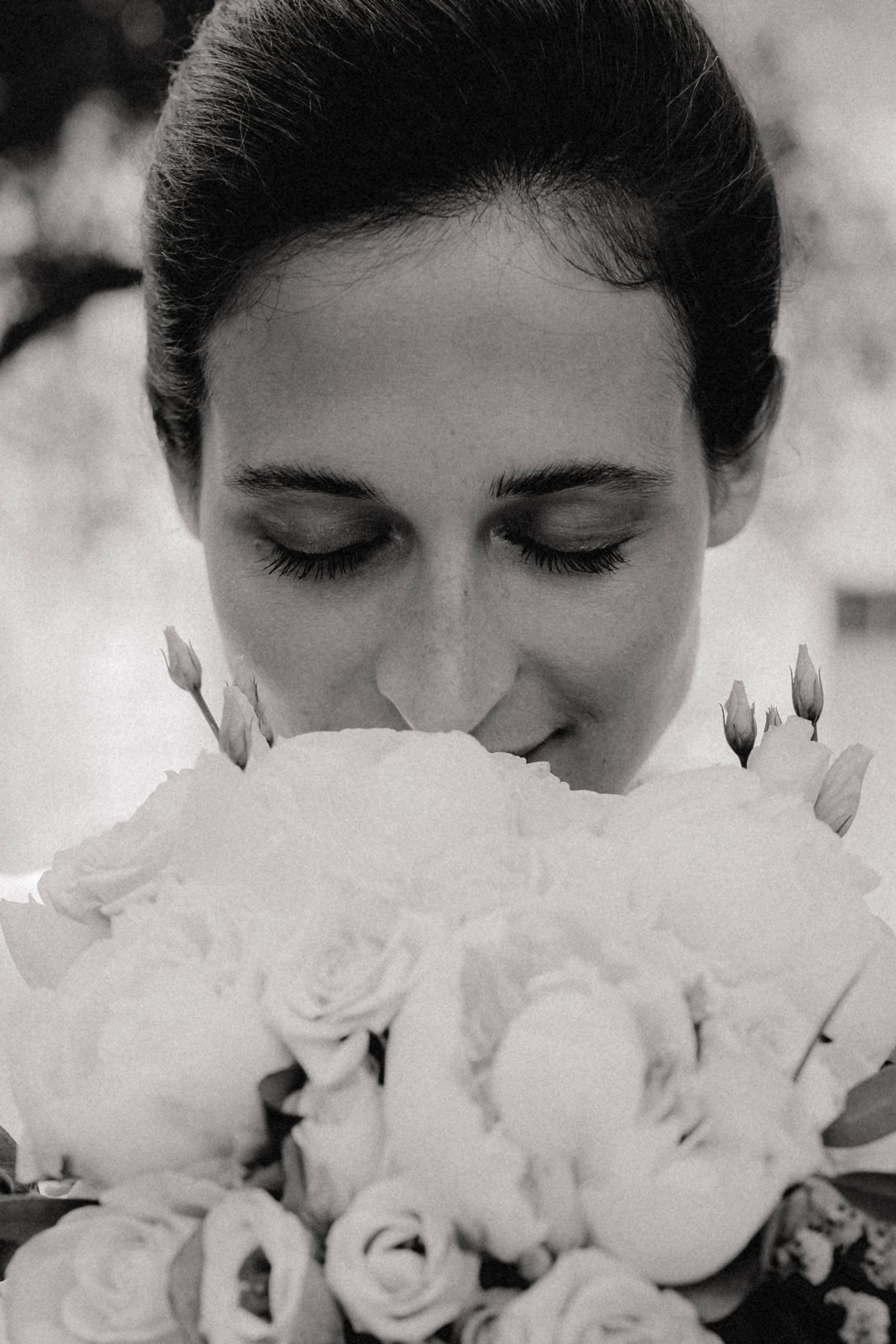 Black and white close-up of bride smelling white rose wedding bouquet with eyes closed.