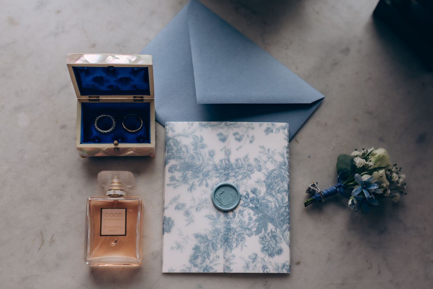 Flat-lay de mariage élégant avec alliances en or dans une boîte en velours bleu, parfum Chanel, papeterie florale avec sceau de cire