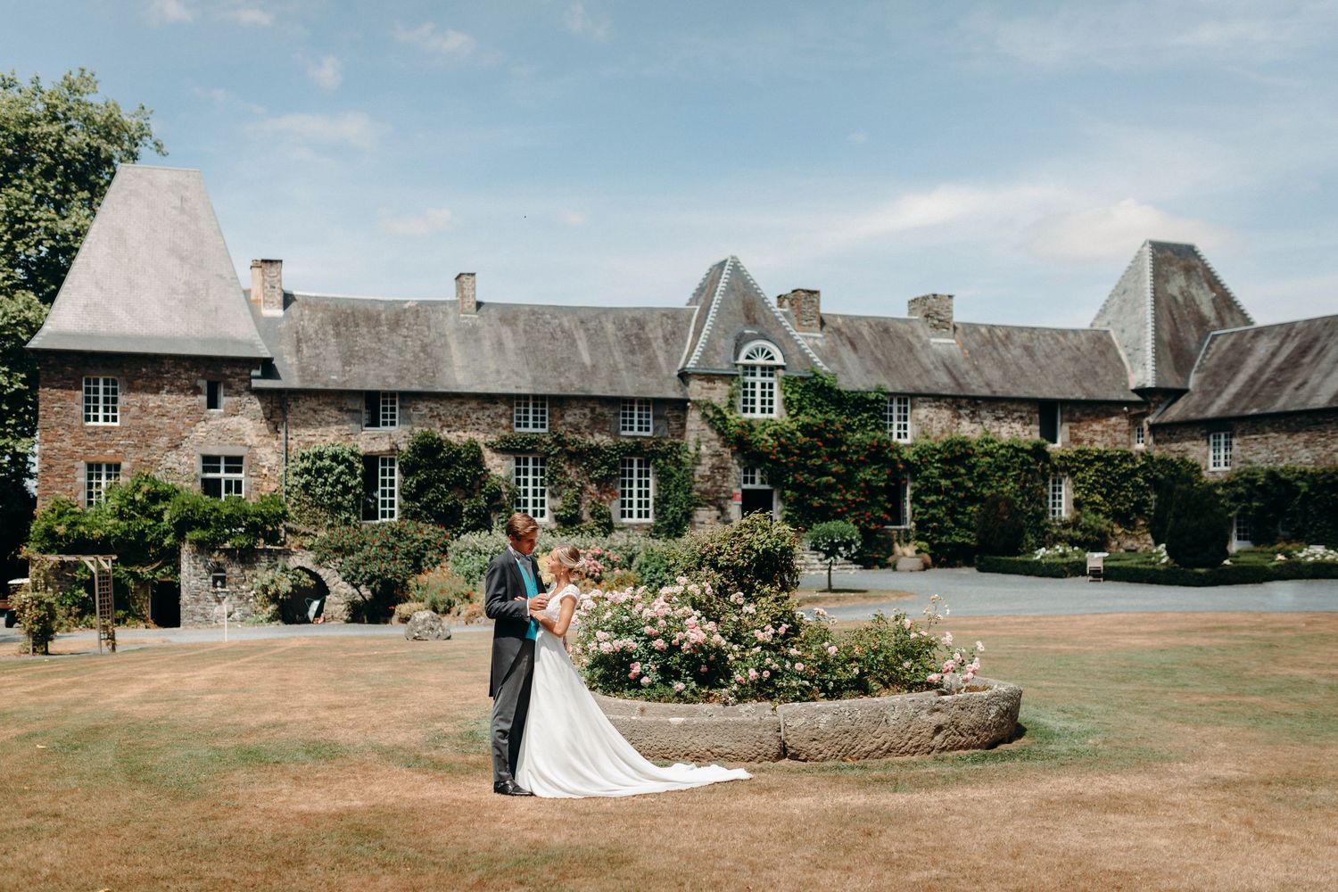 La mariée et le marié s'embrassent dans le jardin luxuriant d'un élégant manoir en pierre le jour ensoleillé du mariage.