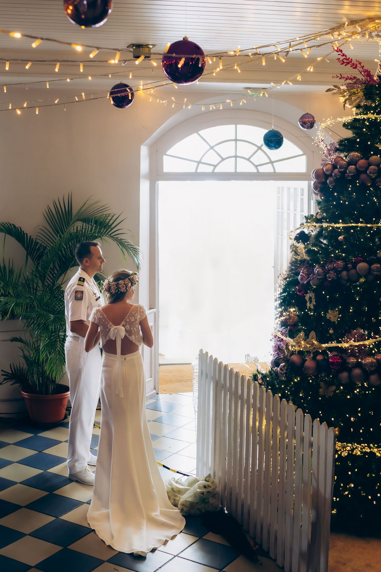La mariée et le marié se tiennent ensemble près d'un sapin de Noël décoré dans un lieu élégant.