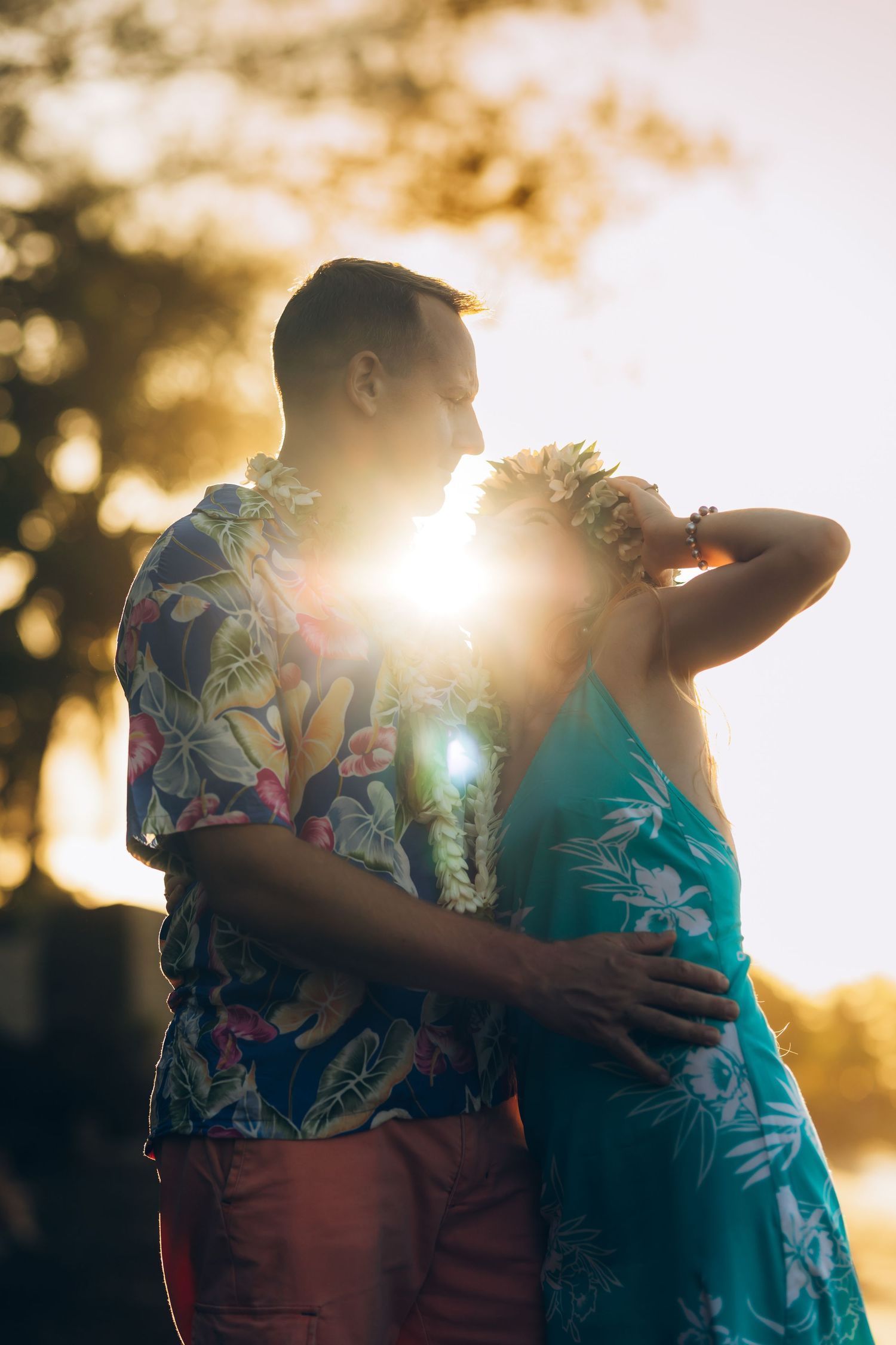 Couple s'embrassant au coucher de soleil doré avec des leis hawaïens tropicales et des chemises à fleurs, en contre-jour