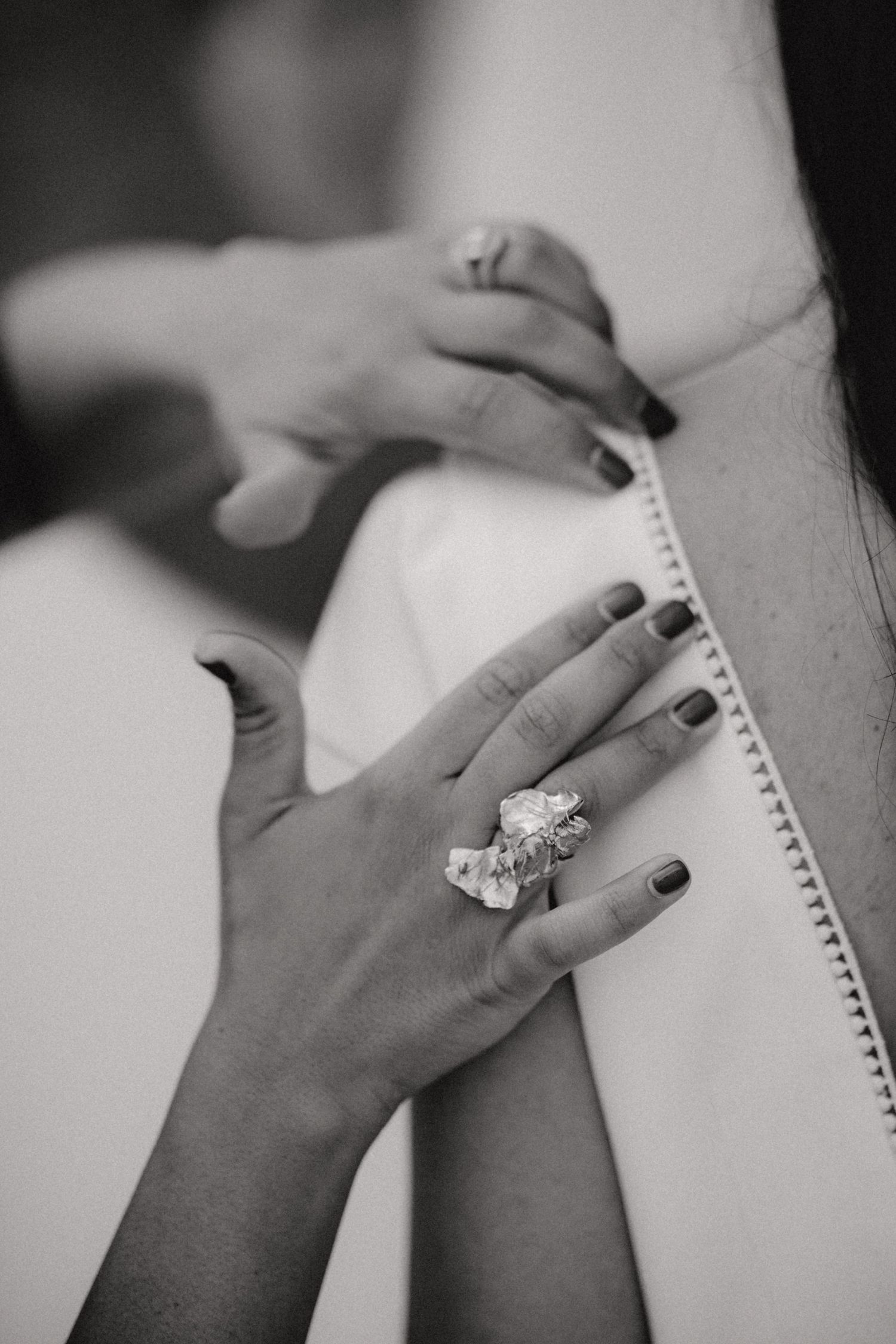 Black and white close-up of hands with statement diamond ring adjusting bridal wedding dress.