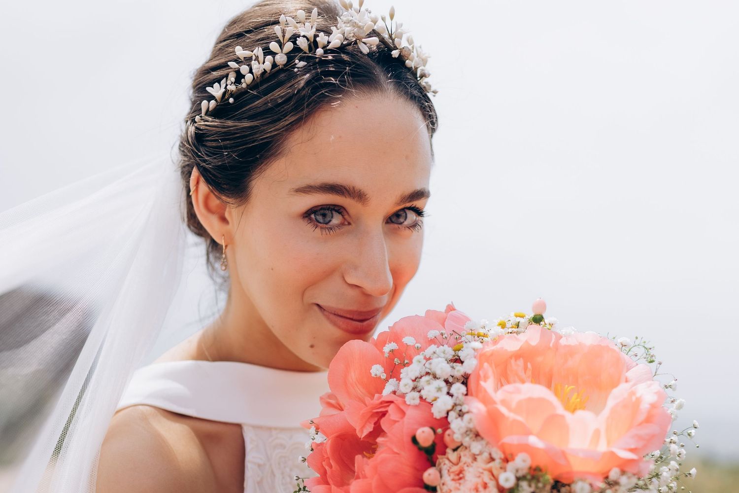 Mariée tenant un bouquet de pivoines corail, portant un voile et une couronne de cheveux à fleurs,