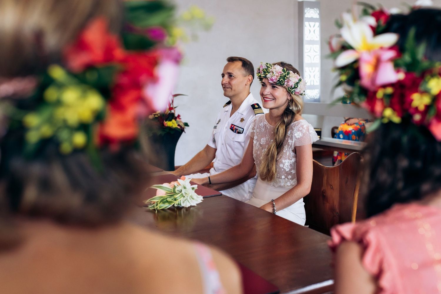 La mariée en couronne florale et le marié en uniforme blanc sont assis ensemble lors de la cérémonie de mariage.