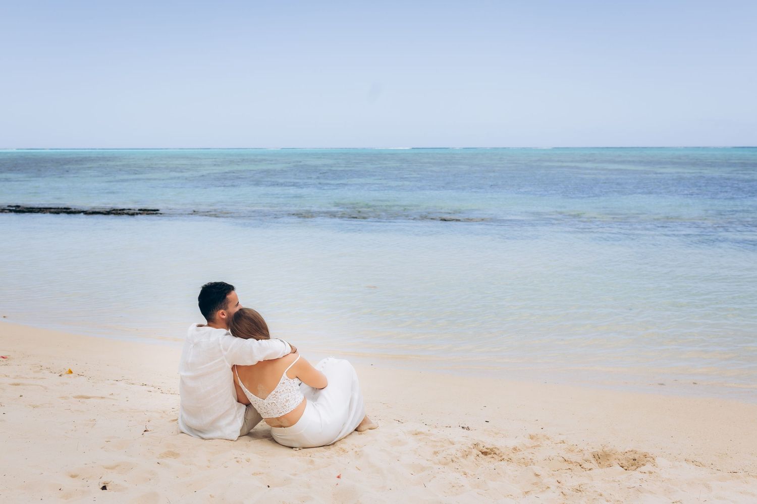 Couple assis ensemble sur une plage de sable blanc regardant l'océan turquoise calme.