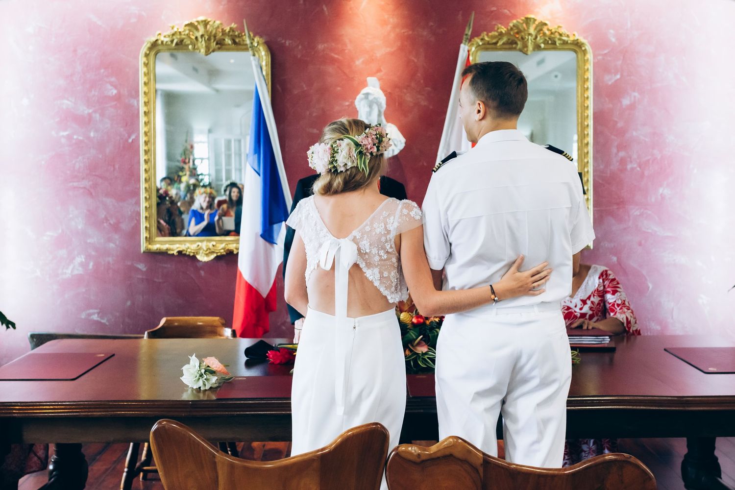 La mariée et le marié se tiennent devant un drapeau français lors de leur cérémonie de mariage civil dans une élégante mairie.