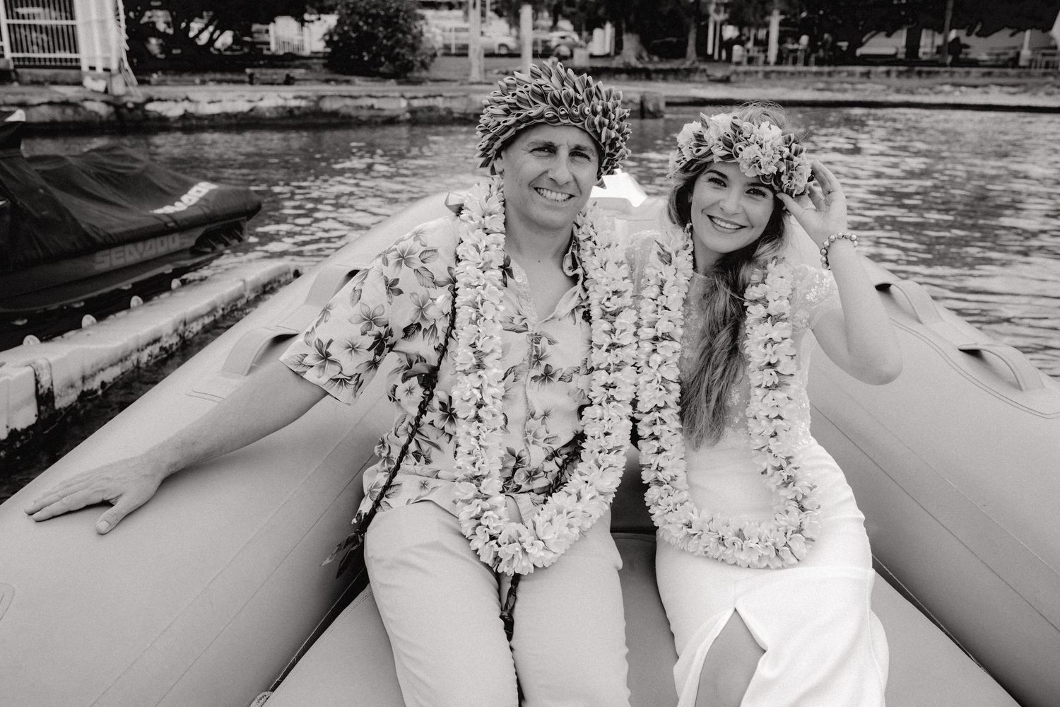 Portrait en noir et blanc de jeunes mariés portant des leis à fleurs tropicales et des coiffes assis sur un bateau.