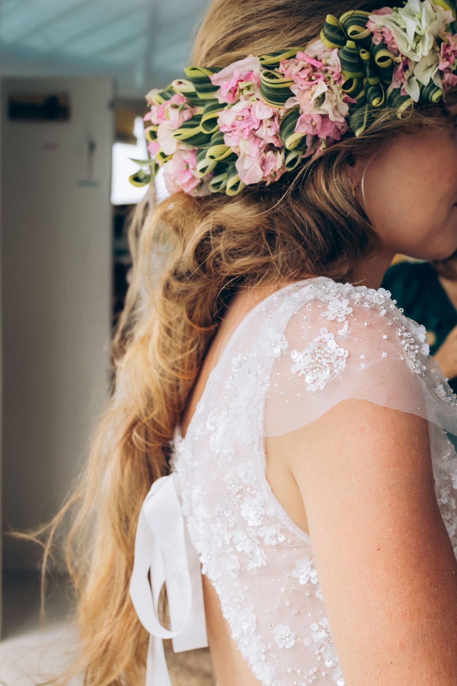 Gros plan de la mariée portant une couronne florale rose avec une robe de mariée en dentelle par derrière.