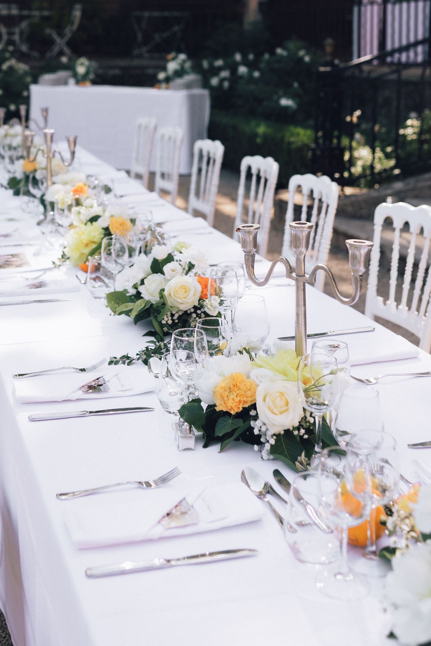 Élégante table de réception de mariage en plein air avec du lin blanc, des candélabres argentés et des centres de table floraux jaunes