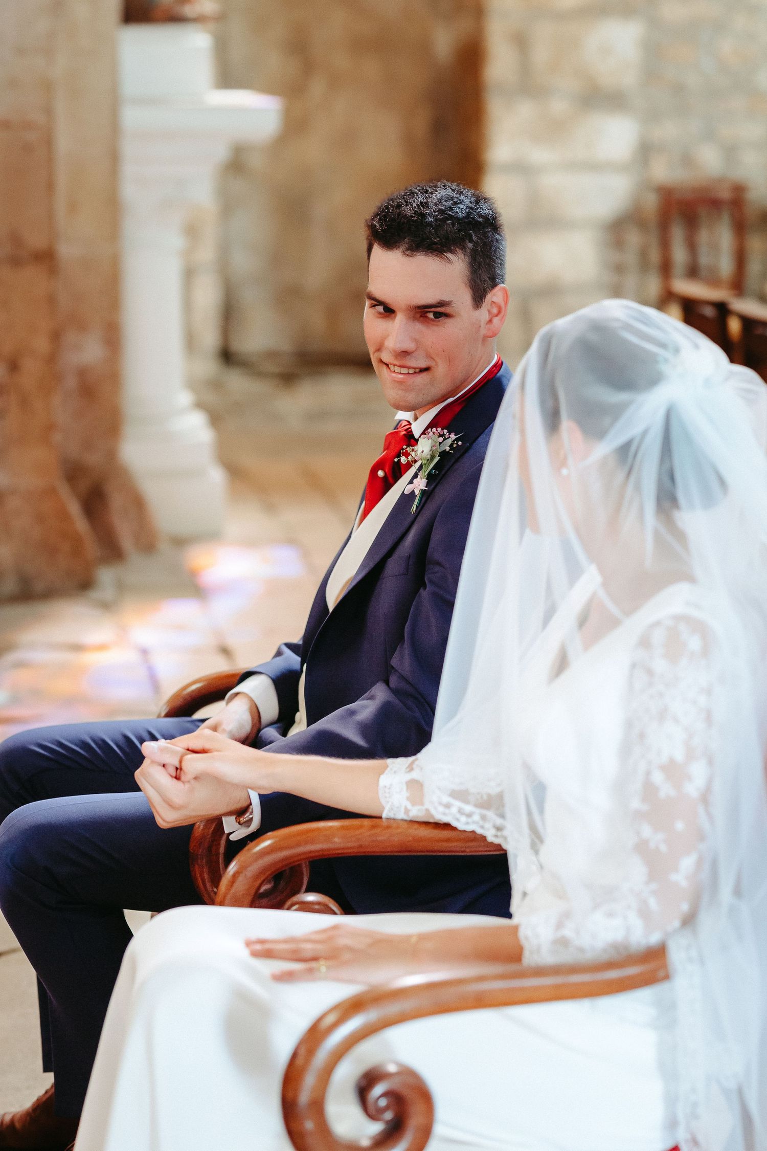 Le marié en costume bleu marine avec nœud papillon rouge tient les mains de la mariée lors de la cérémonie de mariage dans l'église