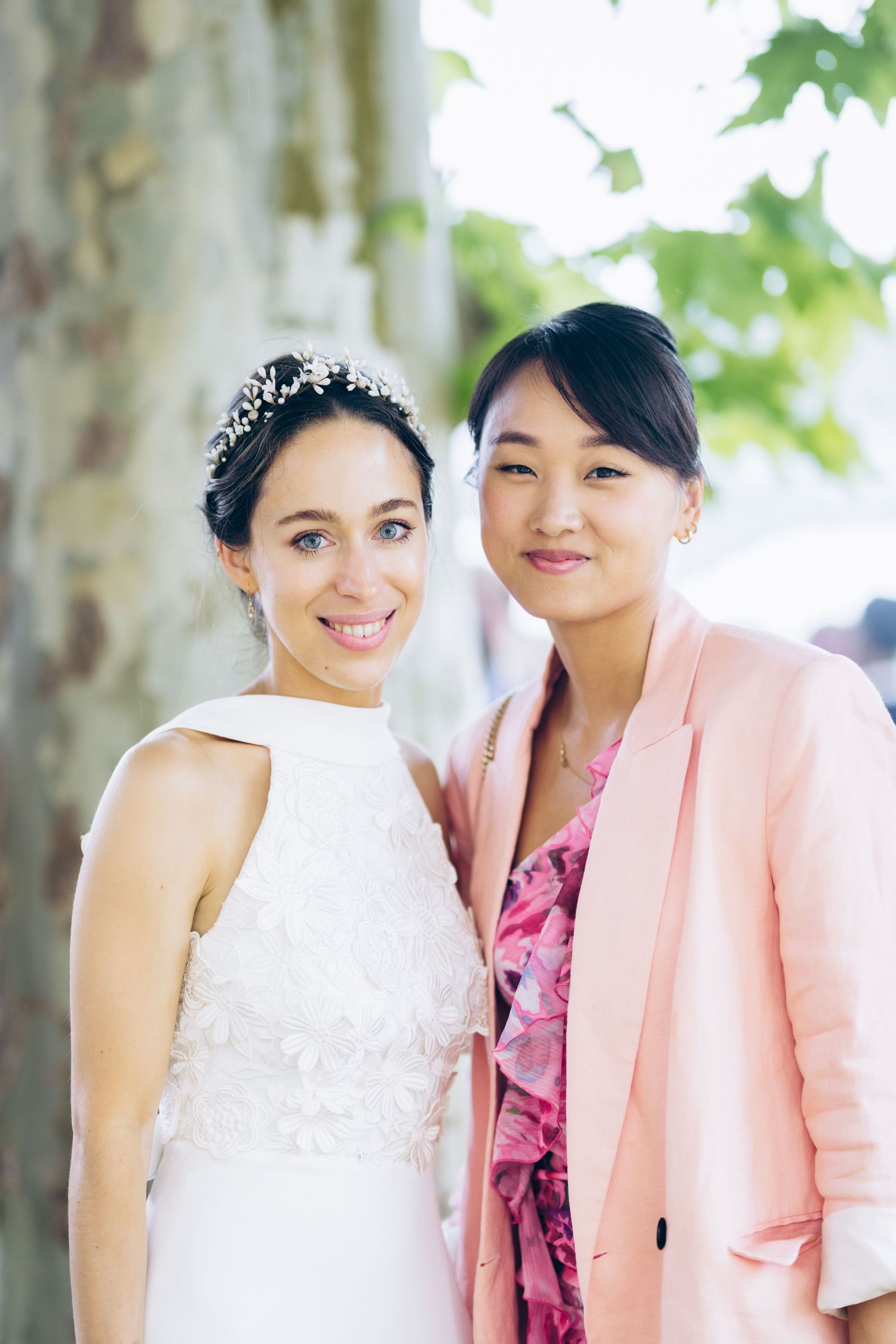 La mariée en robe blanche avec une couronne florale pose avec un invité en blazer rose lors d'une célébration de mariage en plein air.