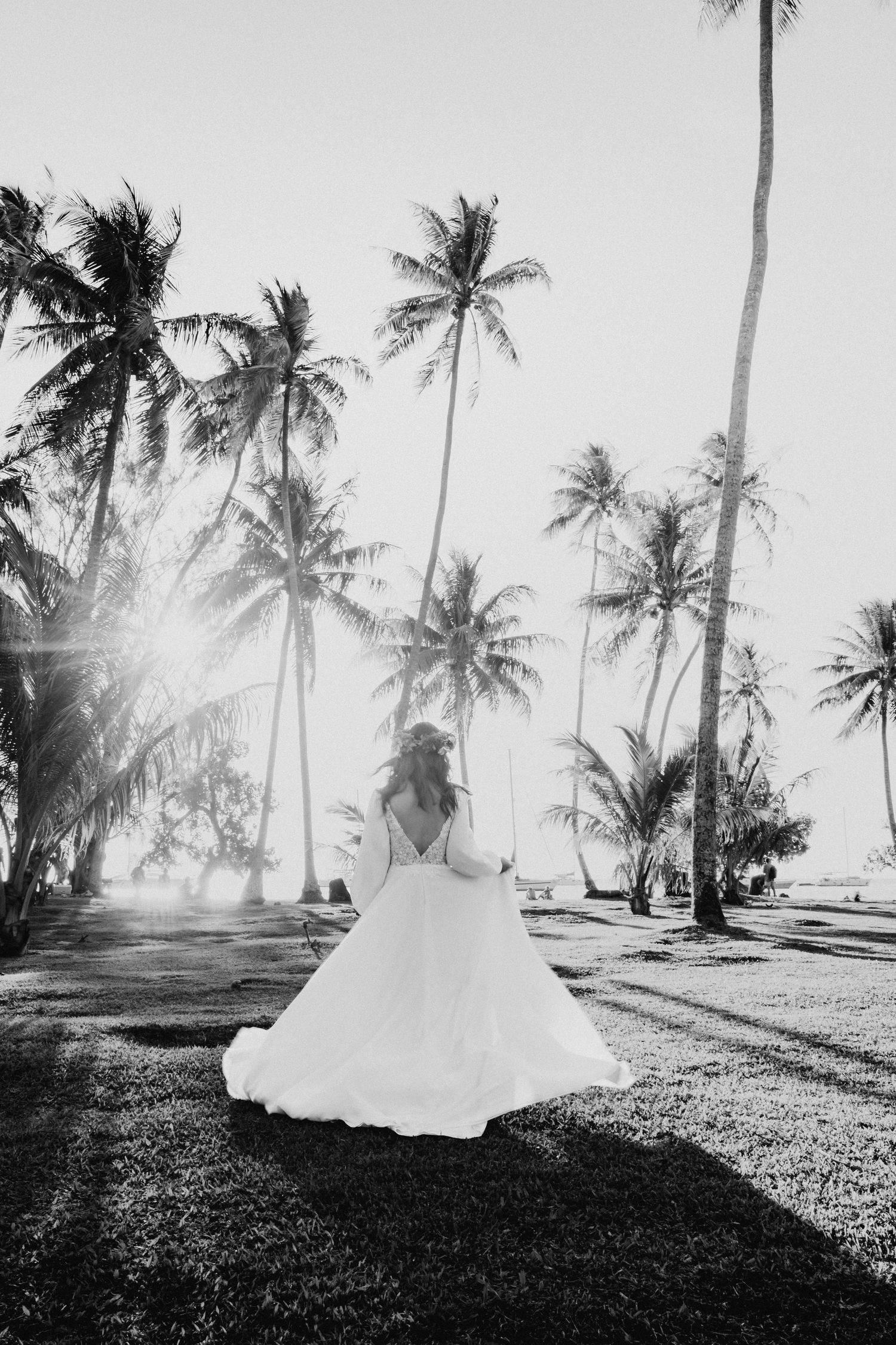 Photo en noir et blanc d'une mariée en robe de mariée marchant à travers les palmiers dans la lumière dorée du soleil.
