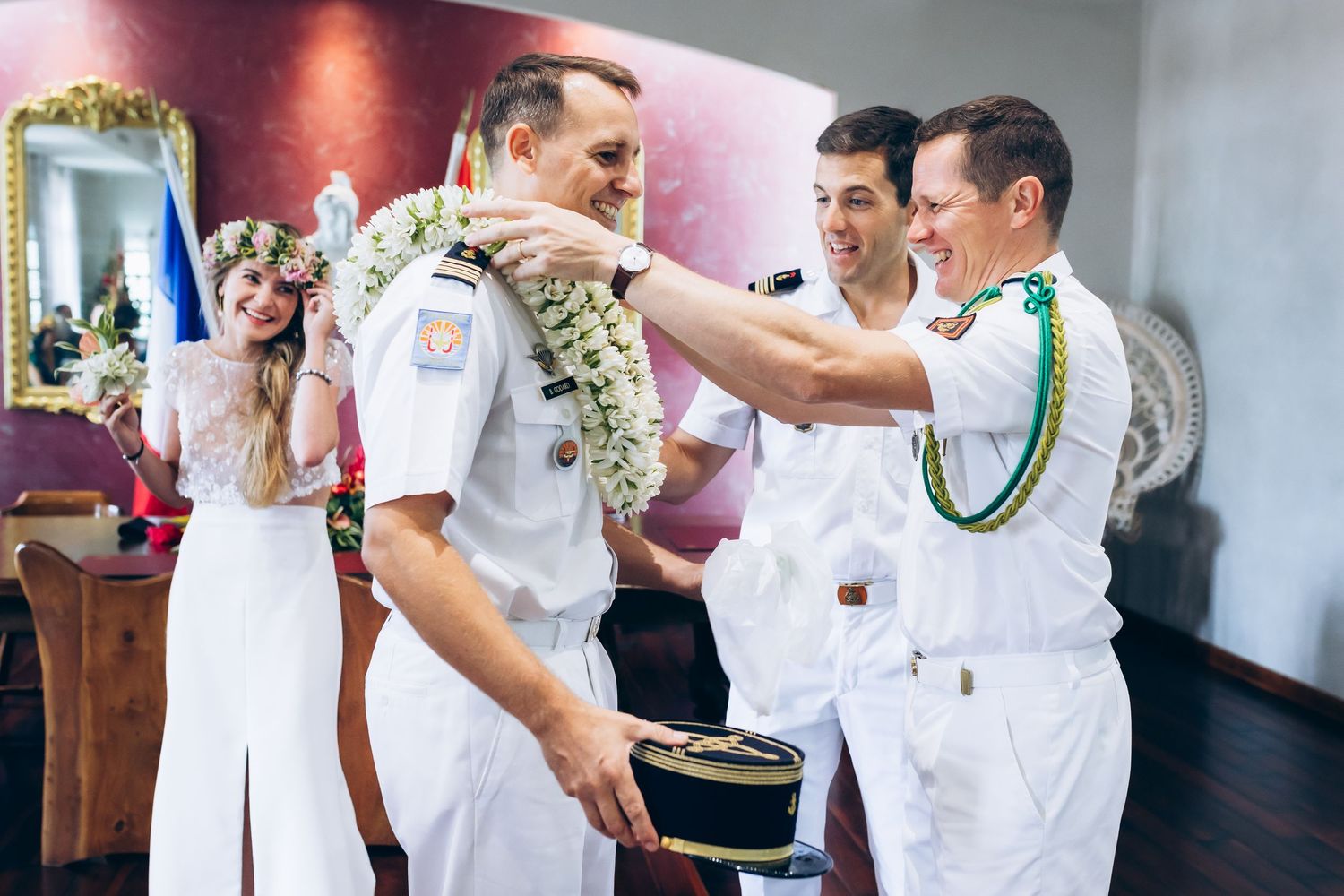 Le marié en uniforme naval blanc reçoit un lei floral traditionnel des garçons d'honneur lors de la célébration du mariage.