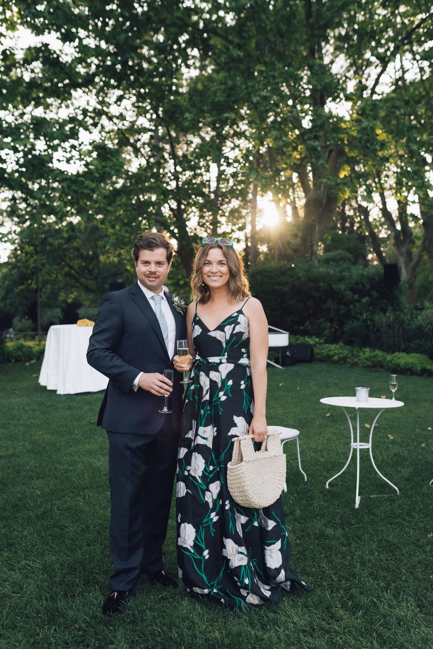 Couple en tenue formelle posant à l'extérieur lors d'une réception de mariage dans le jardin au coucher du soleil, femme en robe à fleurs