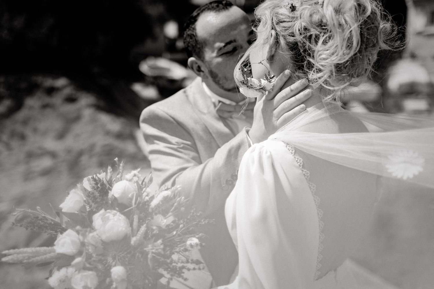Photo de mariage en noir et blanc du marié tenant tendrement le visage de la mariée pour un baiser, avec un bouquet de mariée