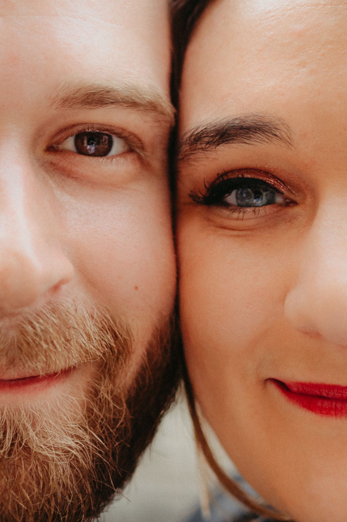 Portrait en gros plan d'un homme barbu et d'une femme aux lèvres rouges et aux yeux bleus souriant ensemble joue contre joue.