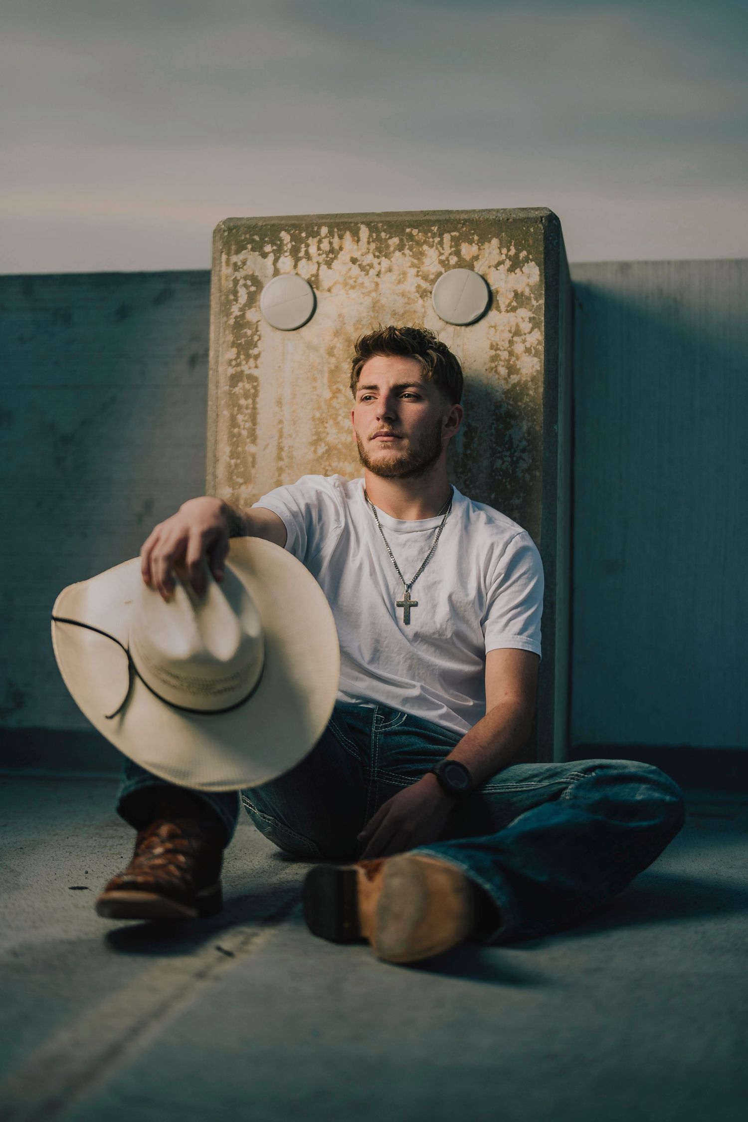 A moody portrait of someone in a white t-shirt holding a cowboy hat against a textured wall. Murfreesboro, Tennessee.