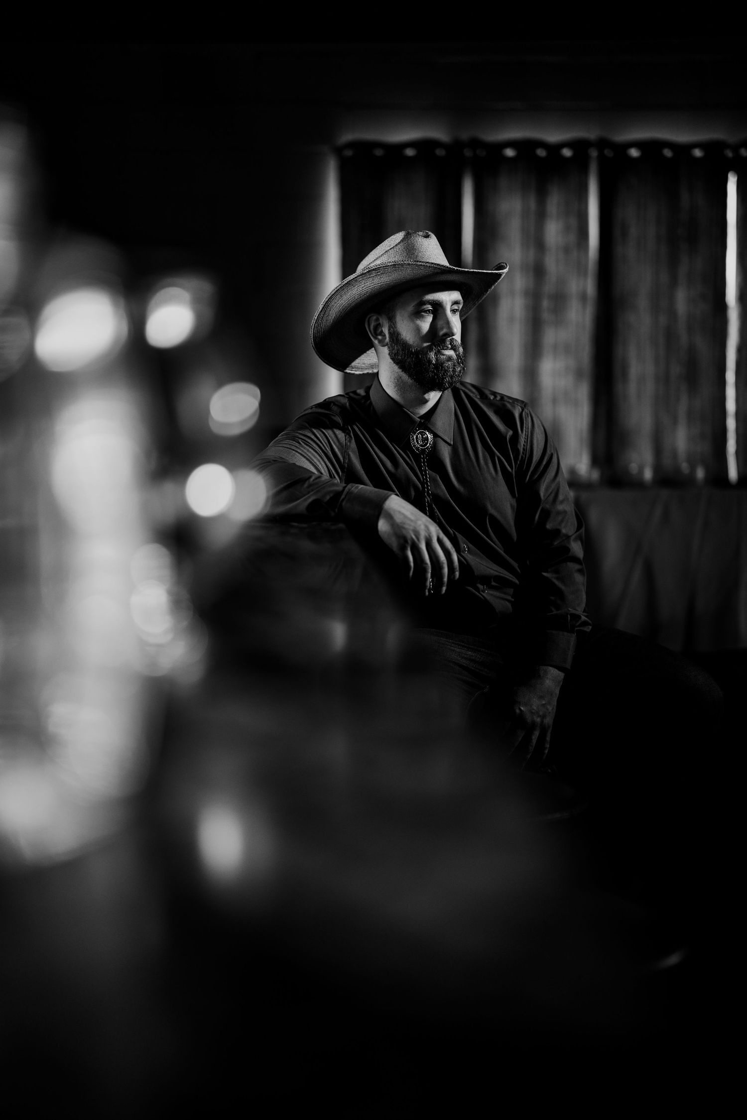 Dramatic black and white portrait of a cowboy in a hat looking contemplative in low light. Milwaukee, Wisconsin.