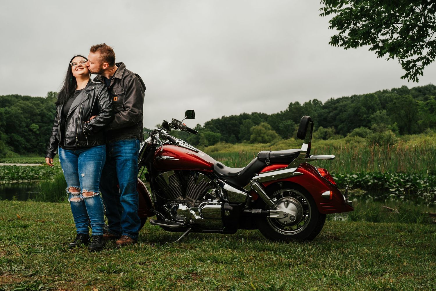 Couple posed with red motorcycle in countryside setting. Indiana.
