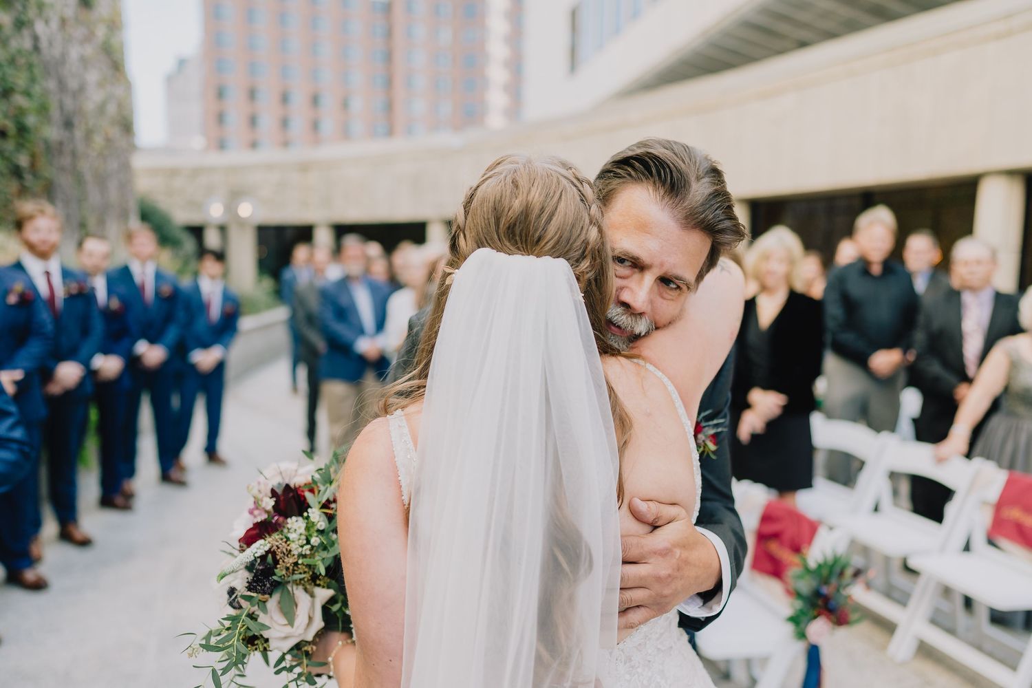 An emotional wedding ceremony moment with guests watching in the background.