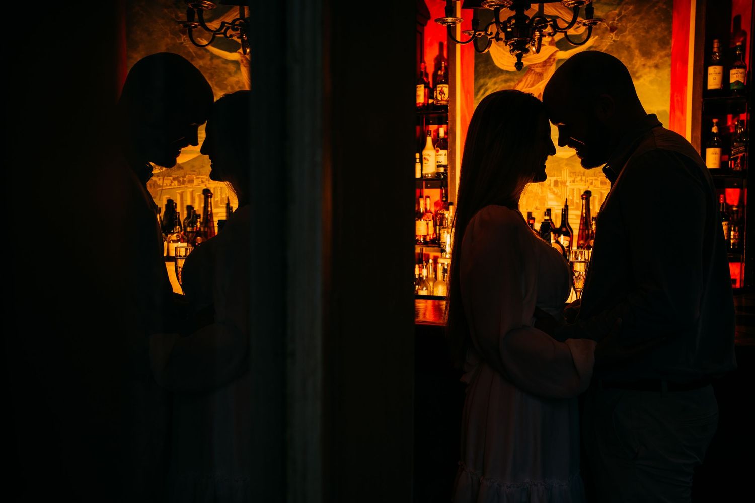 Silhouetted couple embracing in warm atmospheric lighting with ornate chandeliers. Charleston, South Carolina.