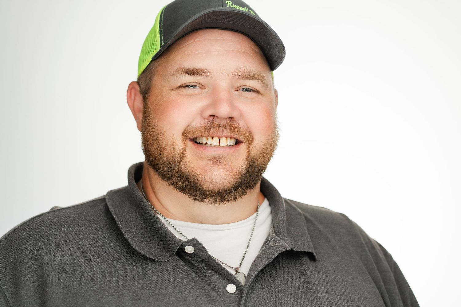 A cheerful man in a baseball cap and gray polo shirt smiles warmly against a white background. Nashville, Tennessee.