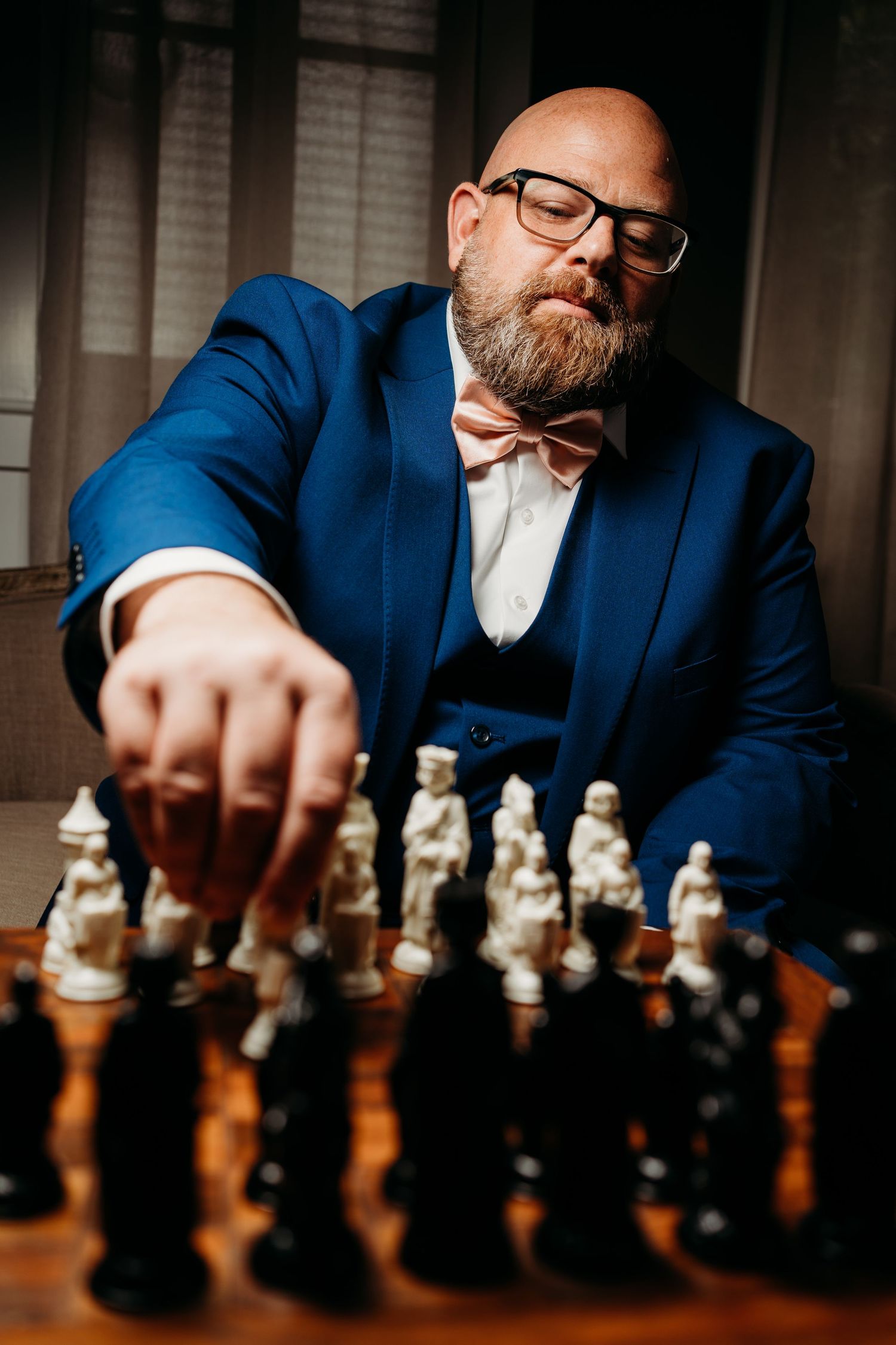 Chess player in blue suit and bow tie makes strategic move with vintage chess pieces on wooden board. Legacy farms, Nashville, Tennessee.