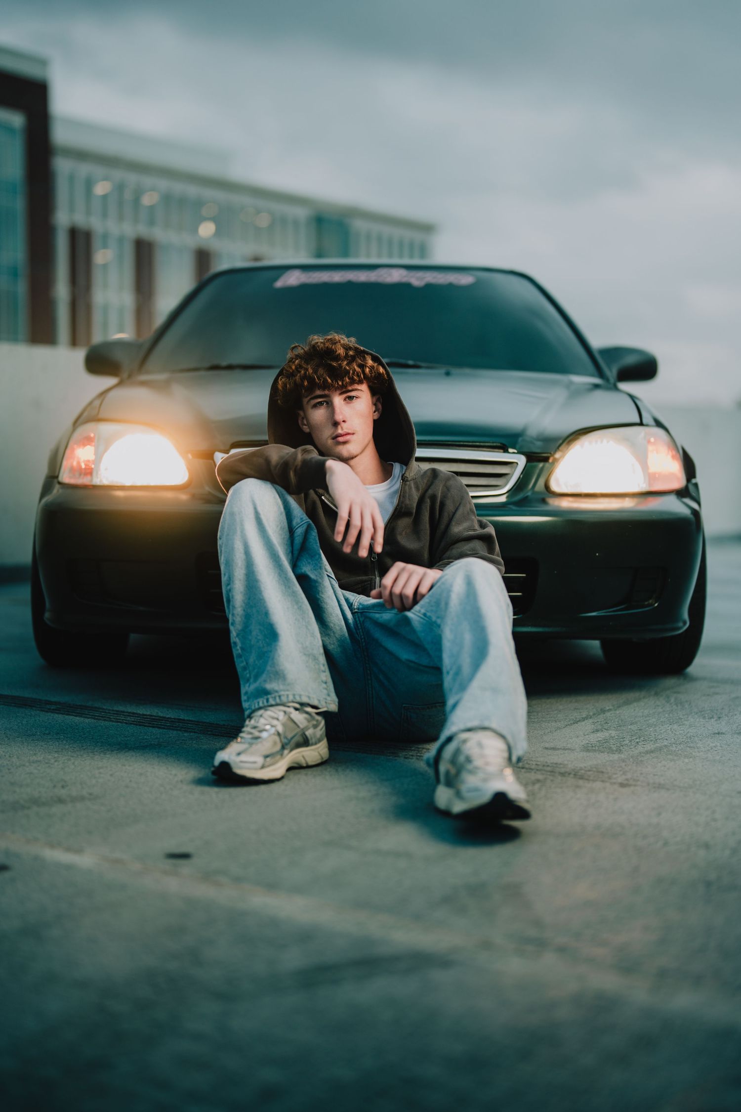 A lifestyle portrait of someone sitting in front of a car with headlights on at dusk. Murfreesboro, Tennessee.