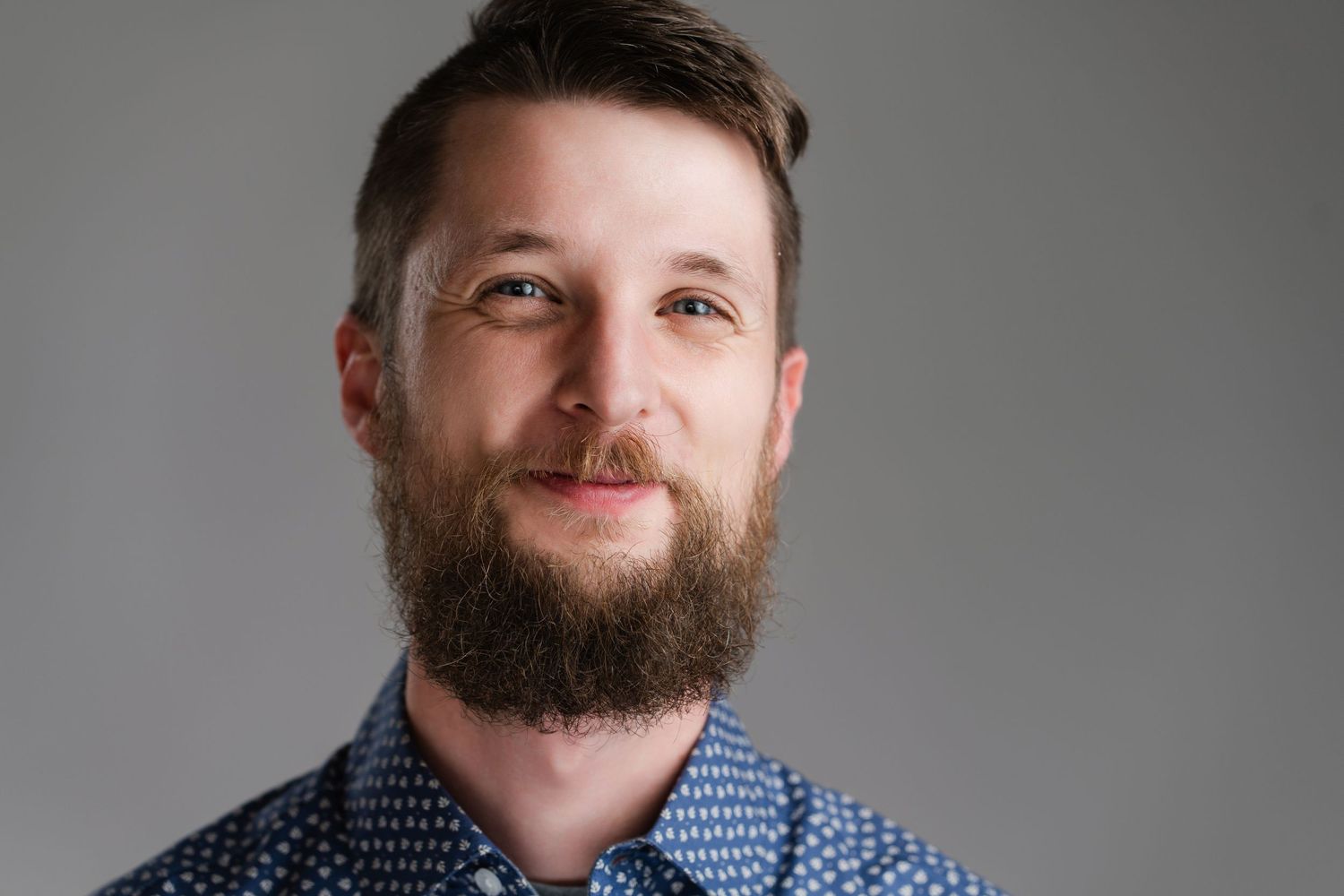 Professional headshot of a bearded person wearing a polka dot shirt against gray background. Nashville, Tennessee.